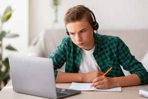Young boy wearing headphones studying on a laptop.