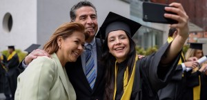 Female graduate in cap and gown taking selfie with parents.