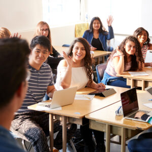 Students in classroom with hands raised.