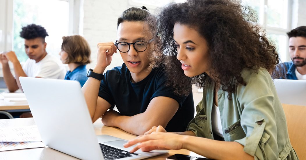 Male and female college students sitting at a table looking at a laptop.