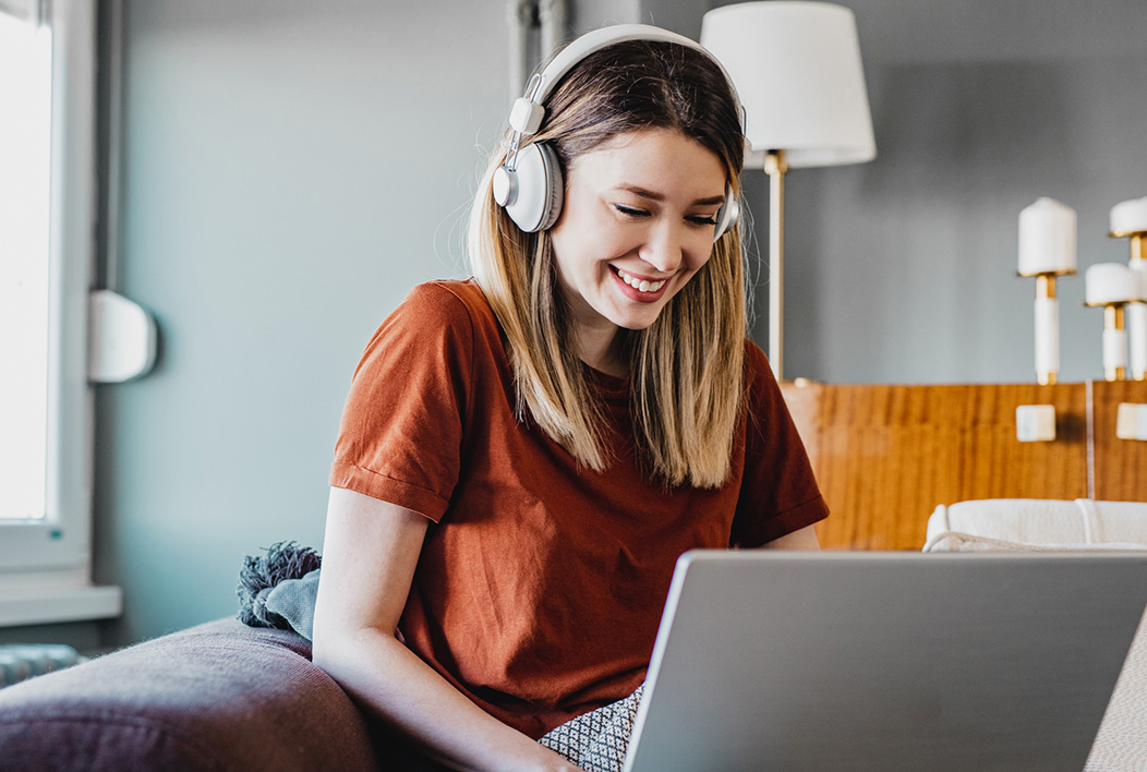 Girl wearing rust colored shirt and headphones working on laptop