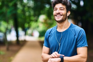 Man smiling wearing headphones holding watch outdoors.