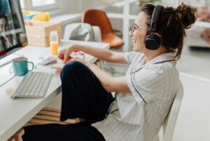 Smiling female college student with dark hair in a messy bun, wearing headphones and participating in a video call.