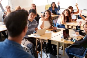 High school students with hands raised smiling at teacher