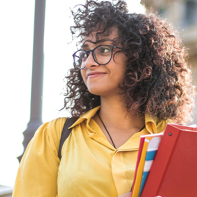 Female college student wearing yellow shirt holding notebooks.