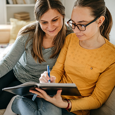 Mother and daughter sitting next to each other on sofa planning college college journey