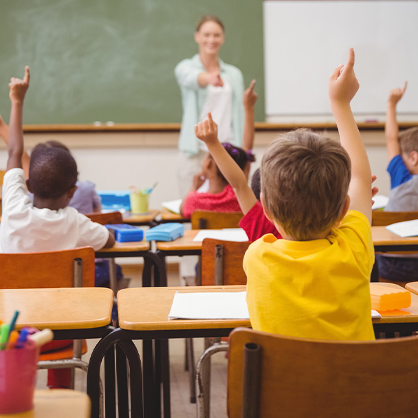 elementary school students with their hands raised and their teacher in a classroom