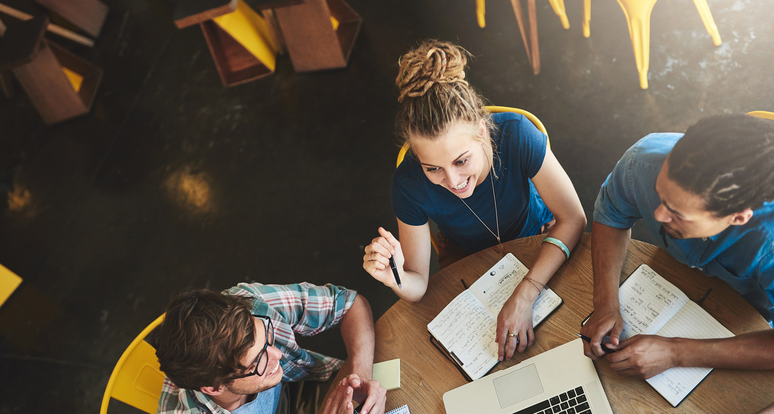 Three college students discussing their education and career journey while sitting at a table with notebooks and a laptop.