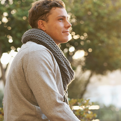 Male college student sitting outside wearing a grey knit scarf and grey long-sleeve t-shirt