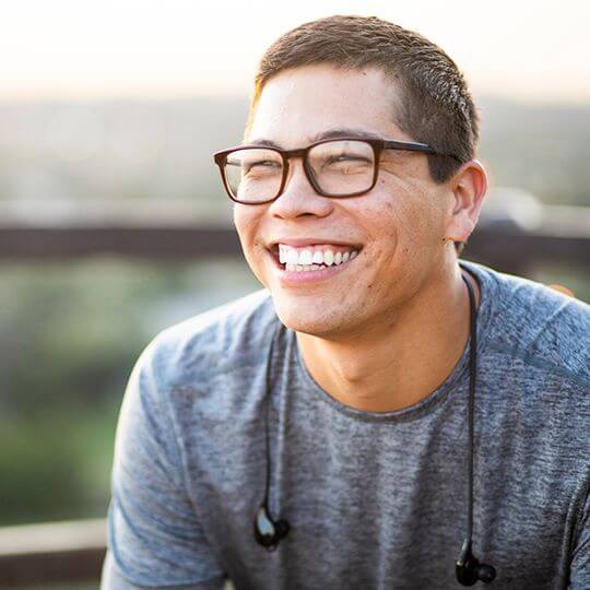 Smiling male college student with glasses sitting outside.