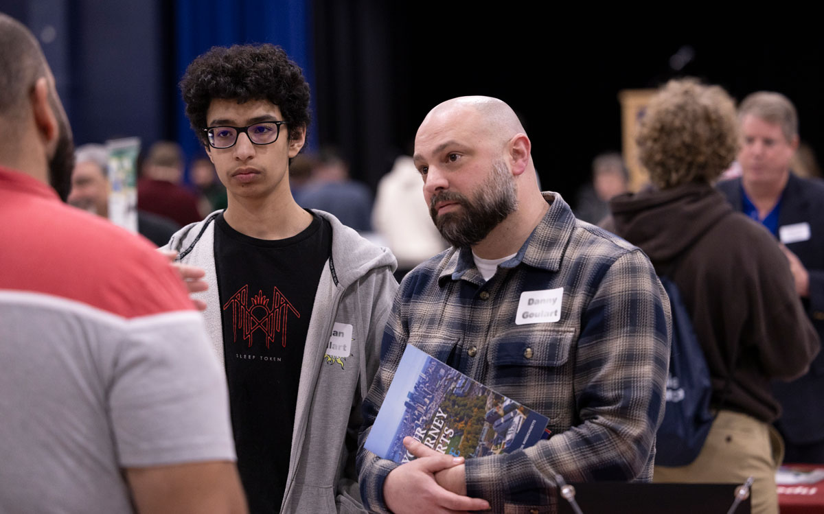 A student and parent stand at a college fair table, getting information from the admission representative.